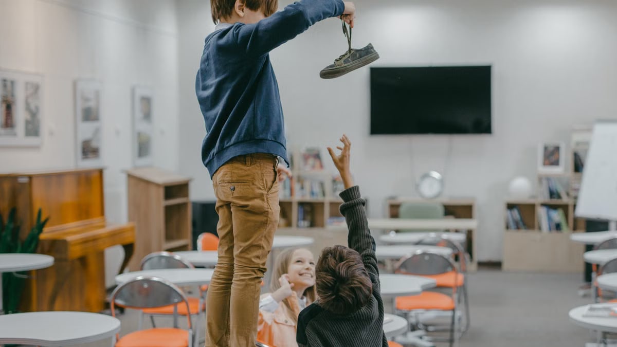 Children interacting in a classroom setting, playfully reaching for an object.